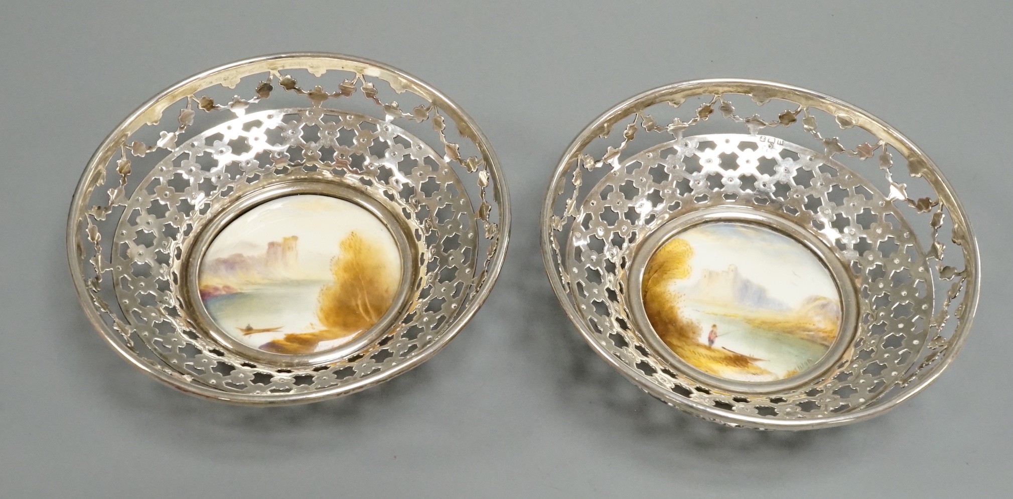 A pair of George V pierced silver mounted Royal Worcester panel bon bon dishes, painted by Raymond Rushton, hallmarked for Sanders & MacKenzie, Birmingham, 1912, diameter 10.5cm.